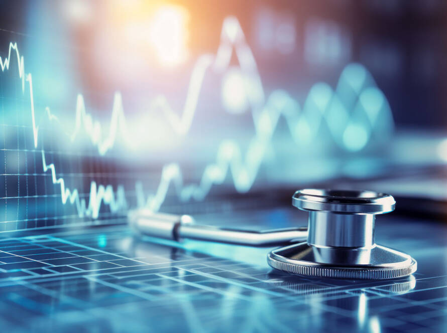 Metallic stethoscope on surface with blurred blue digital graphs and charts, illuminated by soft light from above-left.